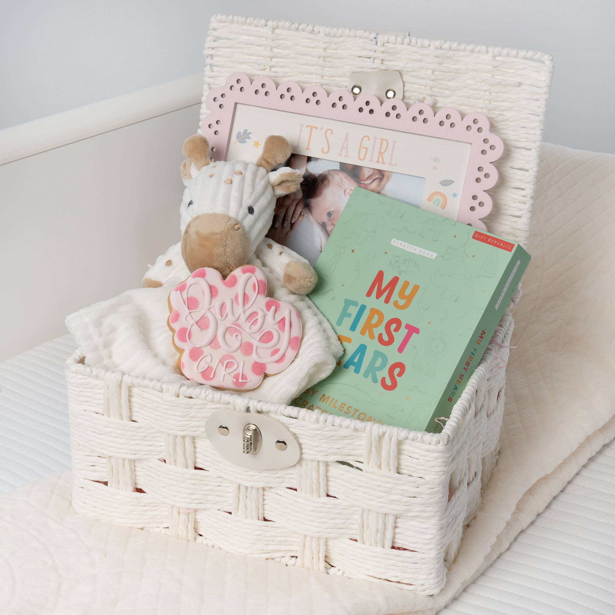 White wicker basket with baby items including a plush toy, baby book, and photo album on a light background.