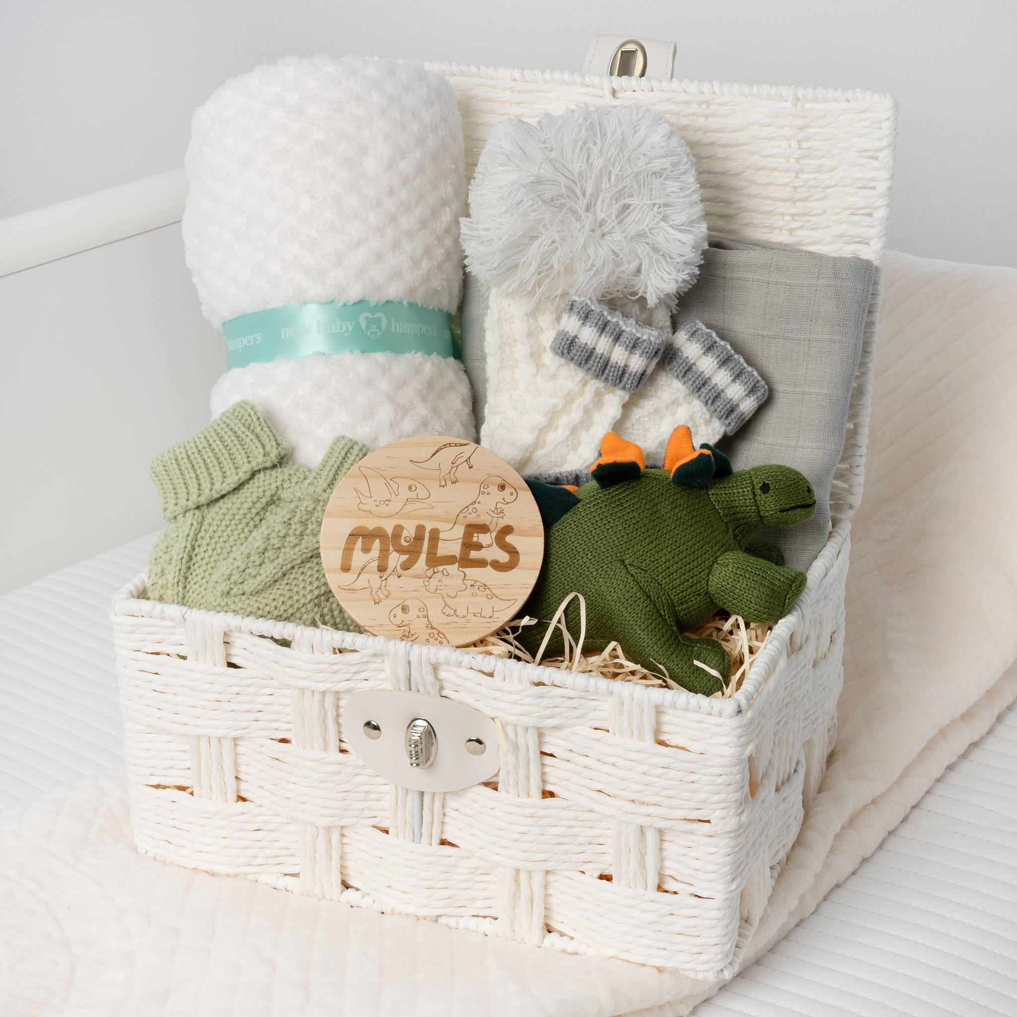 Baby gift basket with plush turtle, blanket, and knitted items on a white surface.