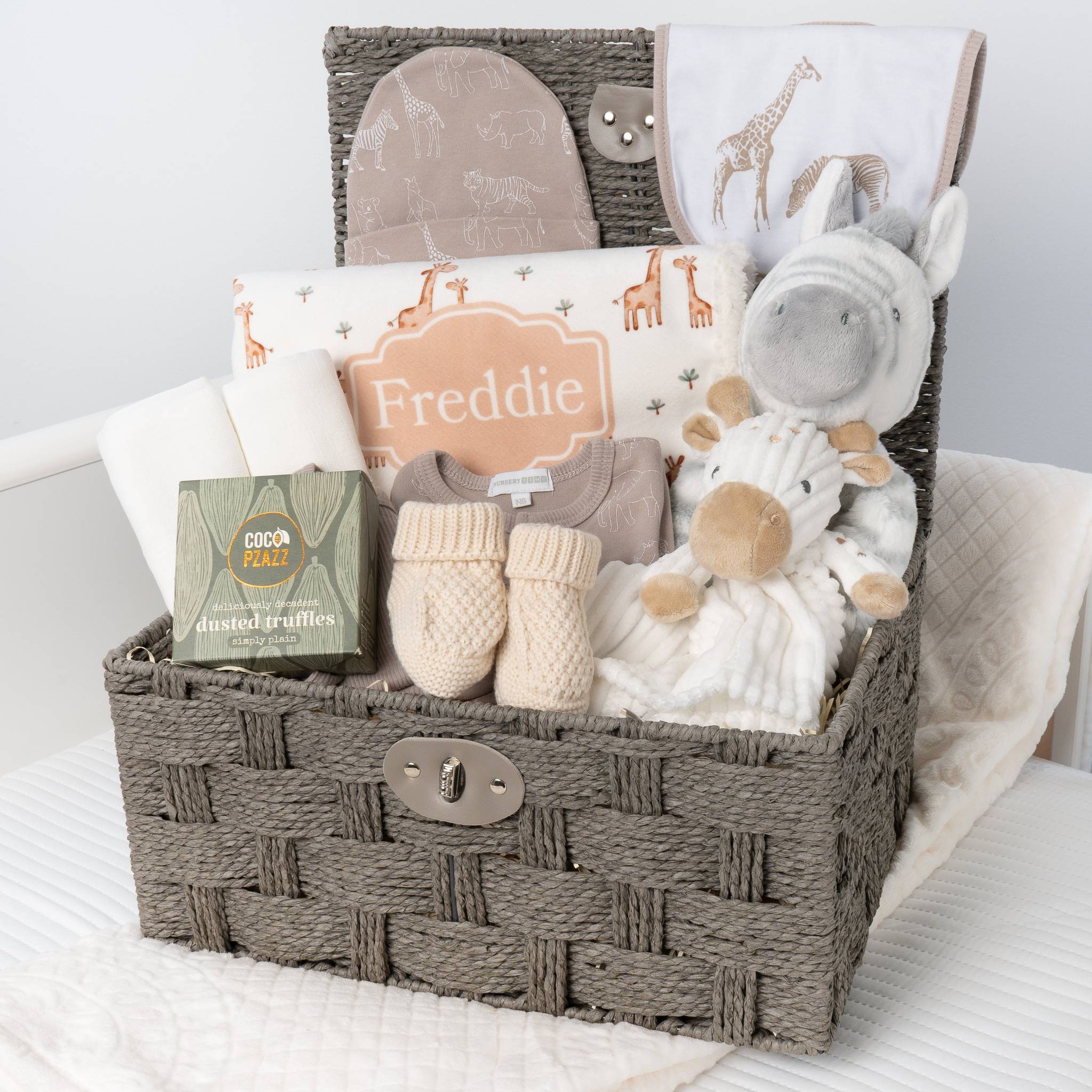 Baby gift basket with plush toys, clothing, and baby products on a white blanket.