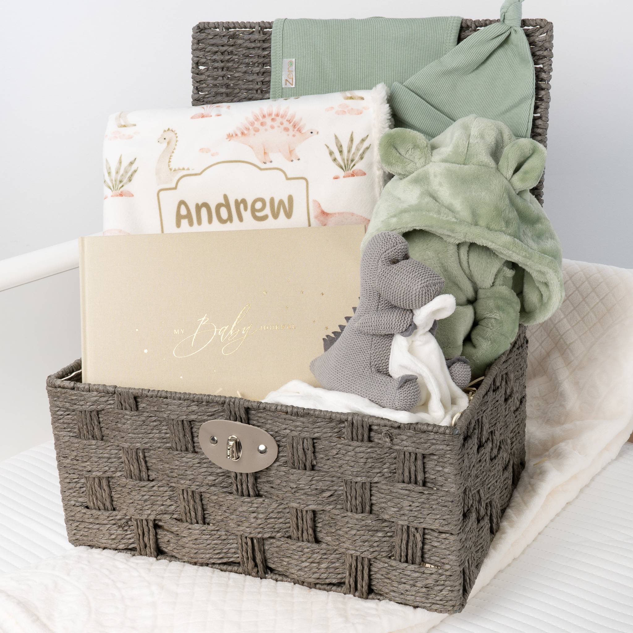 Woven basket with baby items including a blanket, toy, and card on a white surface.