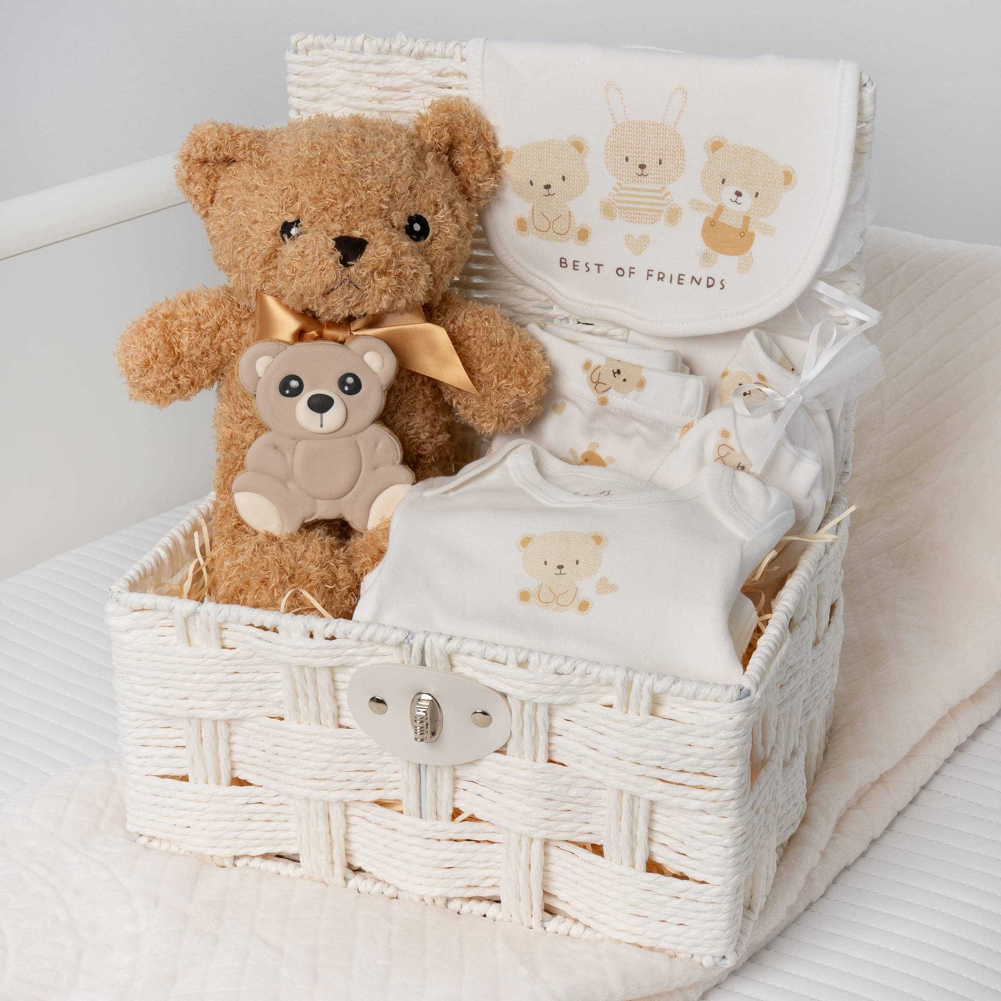 Baby gift basket with teddy bears and baby clothes on a white surface
