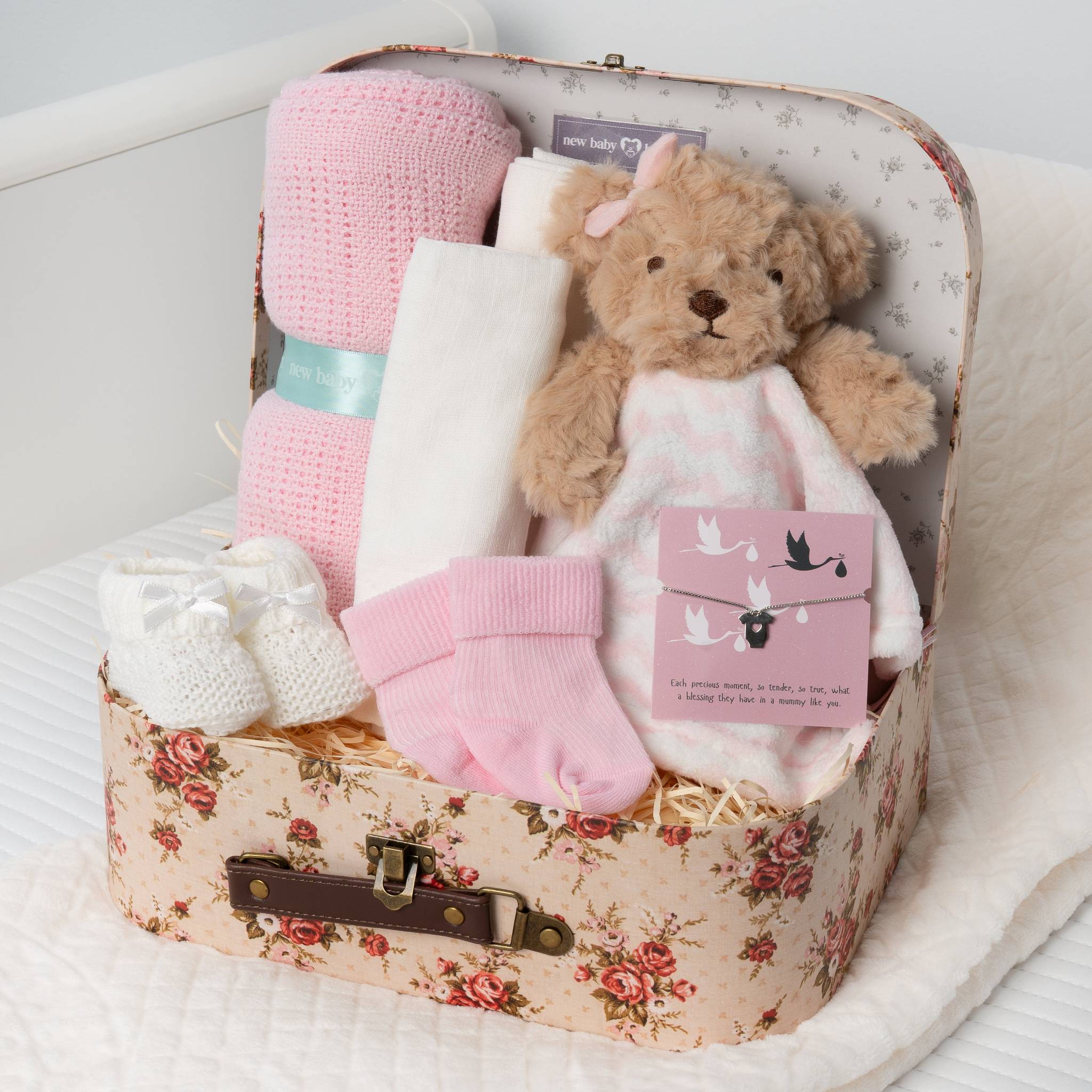 Baby gift set with teddy bear, blanket, and socks in a floral suitcase.