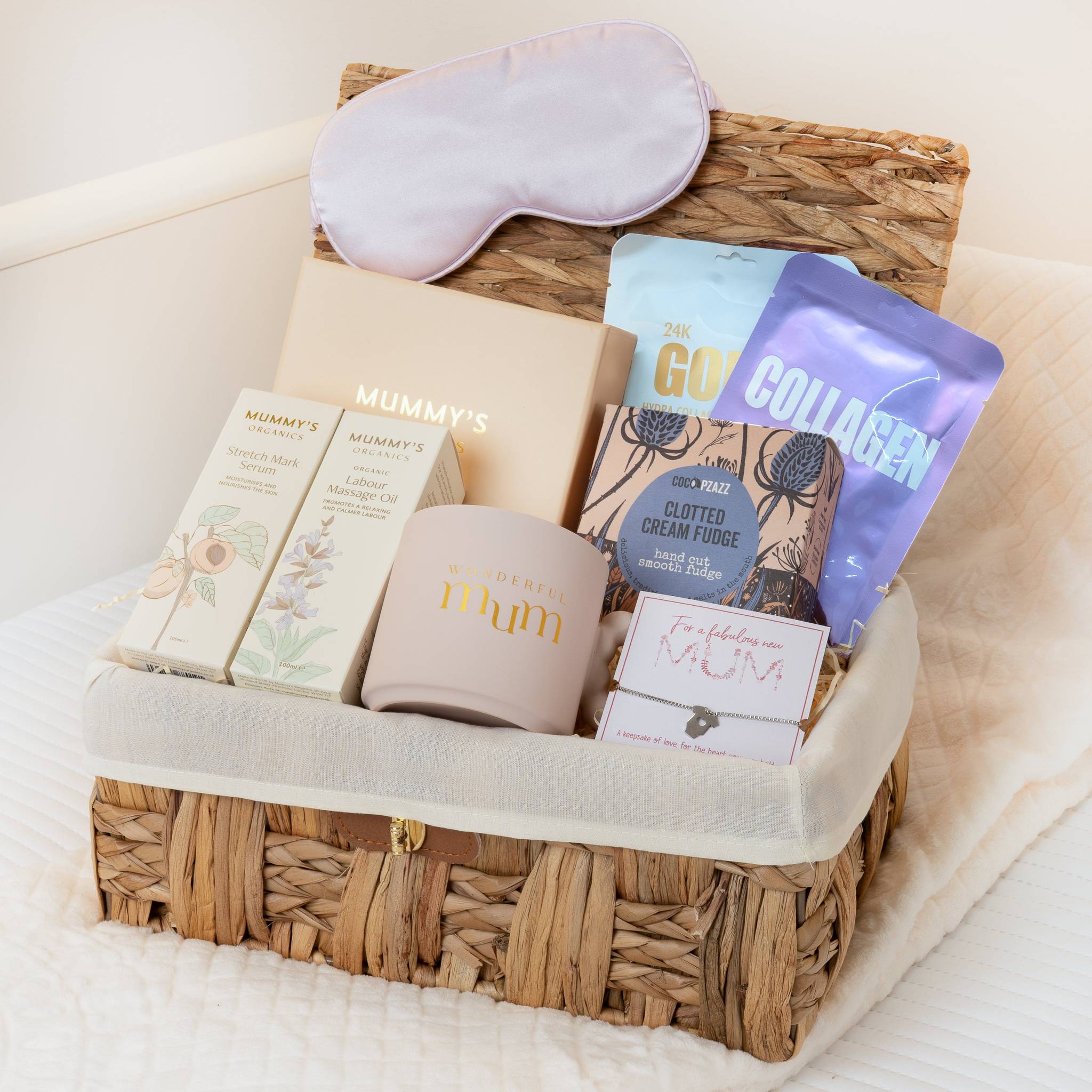 Gift basket with self-care items including a sleep mask, mug, and snacks on a white surface.
